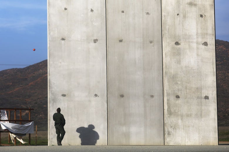 A man in a green uniform stands in front of a concrete wall that appears to be about 30 feet high.